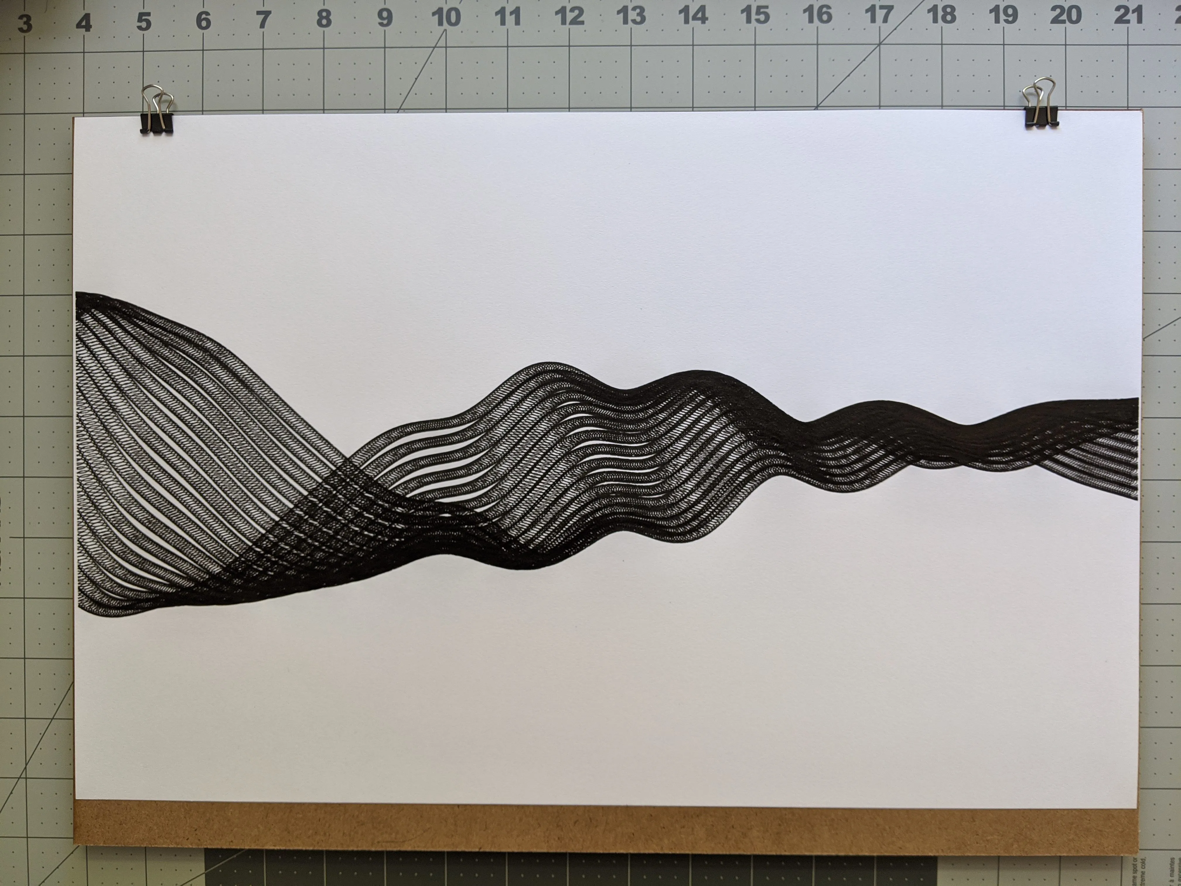 Landscape sheet bulldog-clipped to a board on an inch-ruled cutting mat, a dense black ribbon waving across it