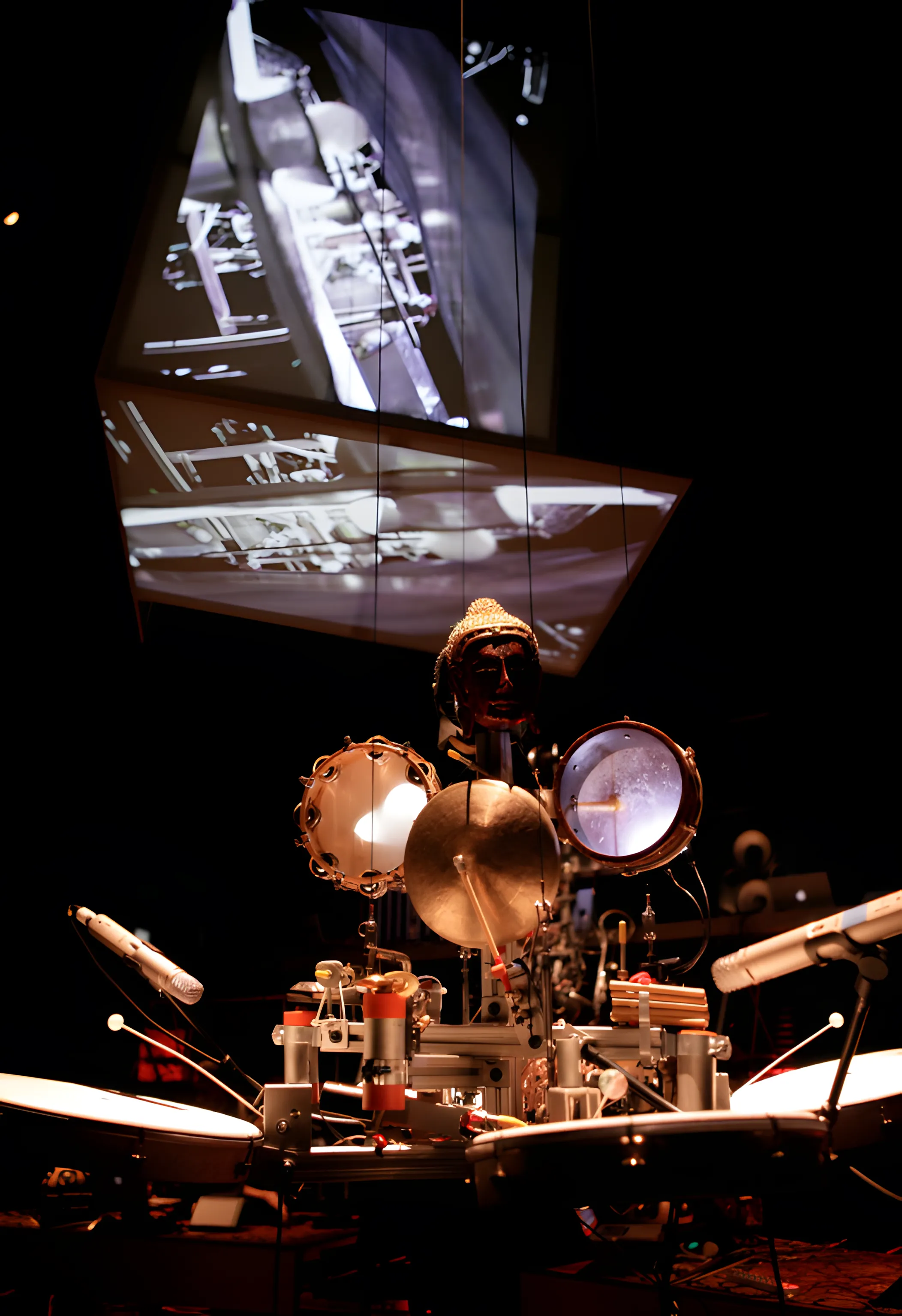 A gilded head mounted above a robotic rig of tambourine, cymbal and snare, microphones angled in from both sides.