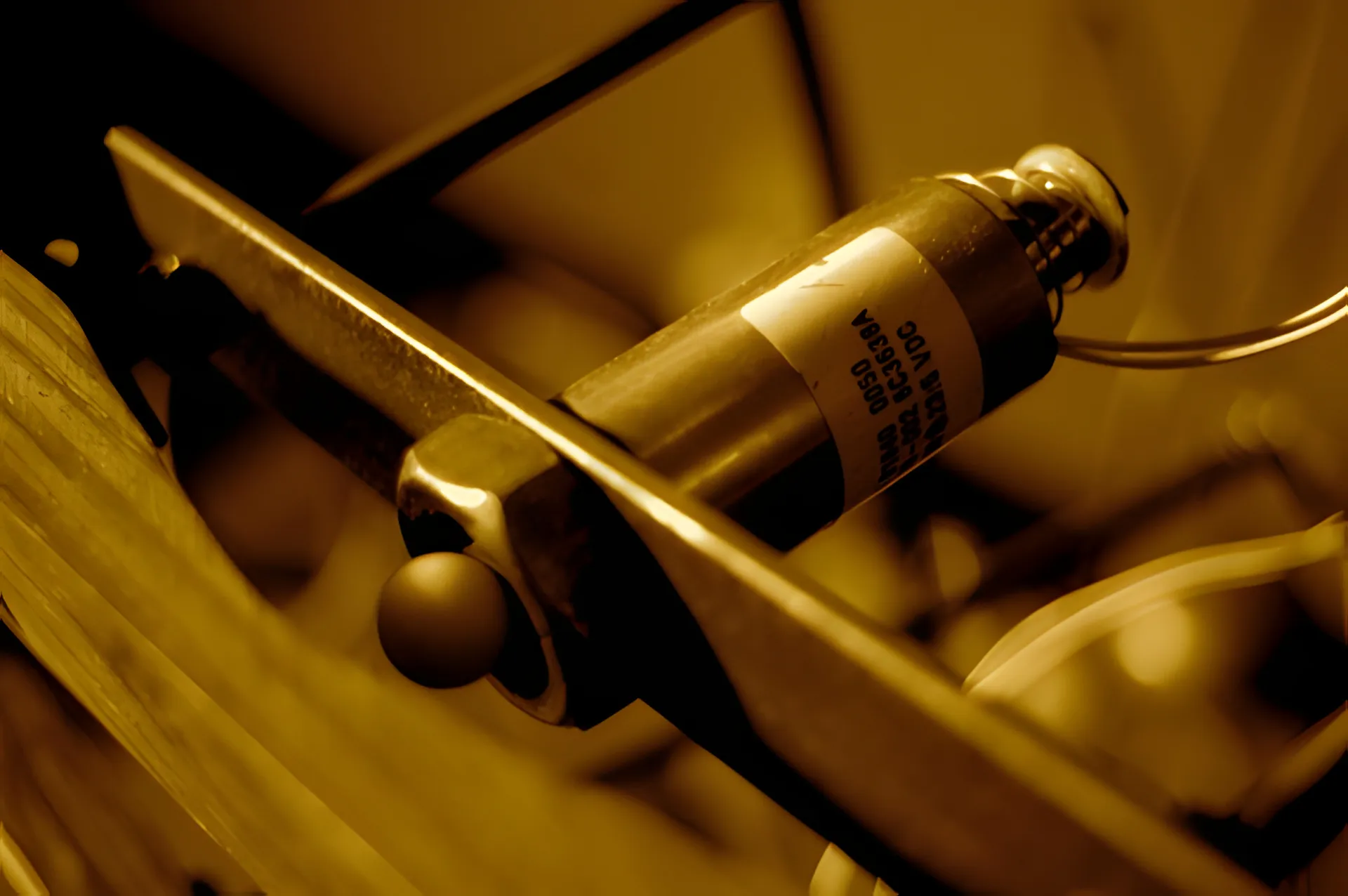 Macro of a labelled solenoid clamped to a steel bracket, its ball-tipped beater resting below